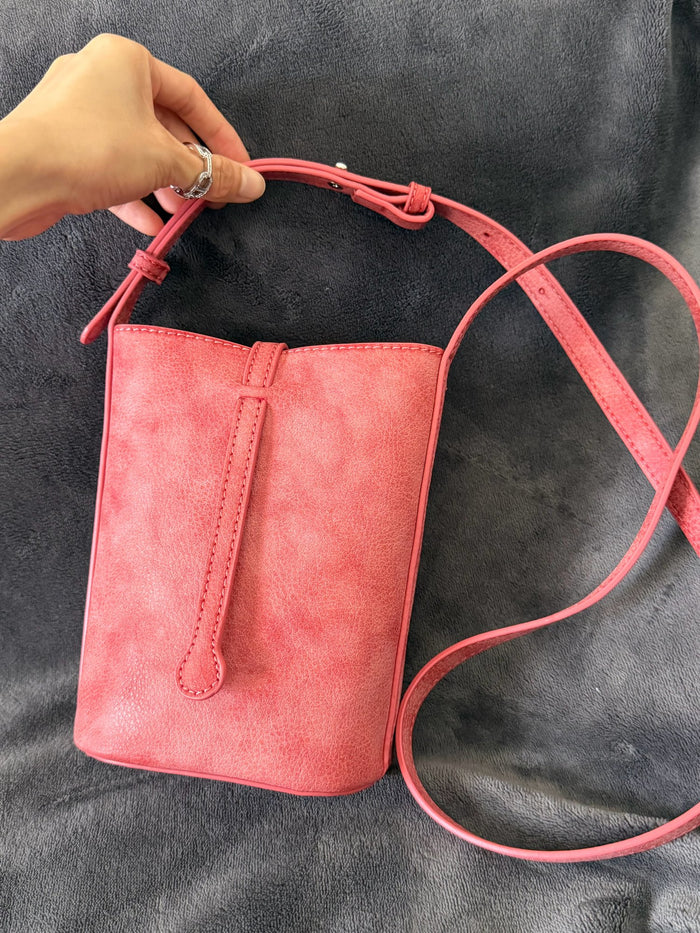 MUGRS Watermelon Red leather phone bag lifted by hand from a grey sofa