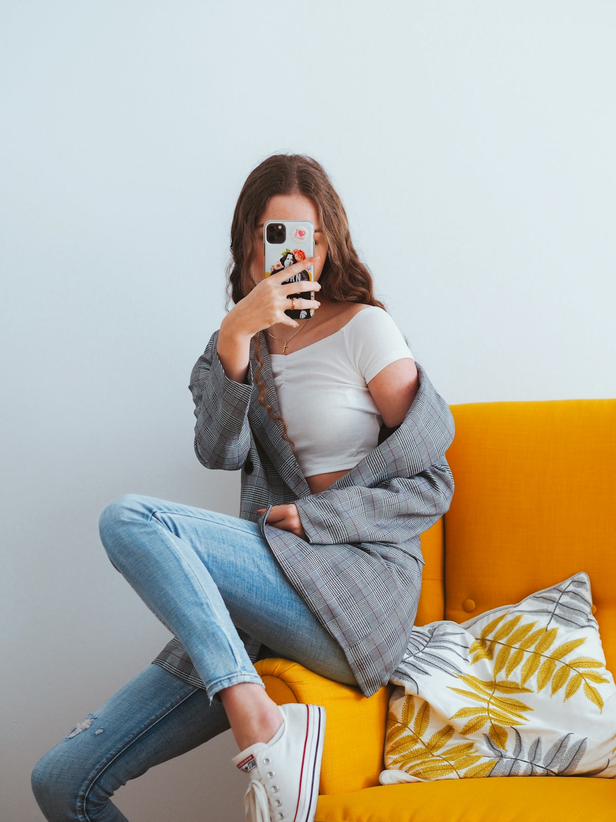 Donna in giubbotto grigio e jeans denim blu seduta su divano giallo