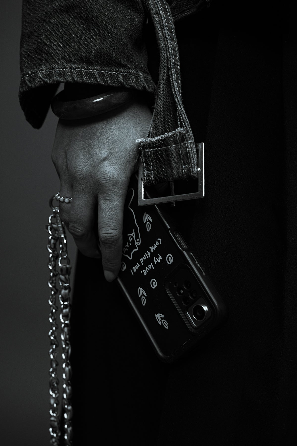 A hand holds a smartphone with a chain strap.