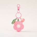 A pink crocheted flower-shaped keychain charm with a white center, green leaf, and small pink bell, attached to a pink ring and lobster clasp.