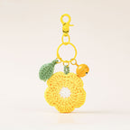 A yellow crochet flower keychain charm with a green leaf, a small yellow bell, and a gold clasp