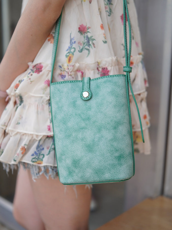 MUGRS green leather phone bag worn over a floral summer dress, close crop at the hip