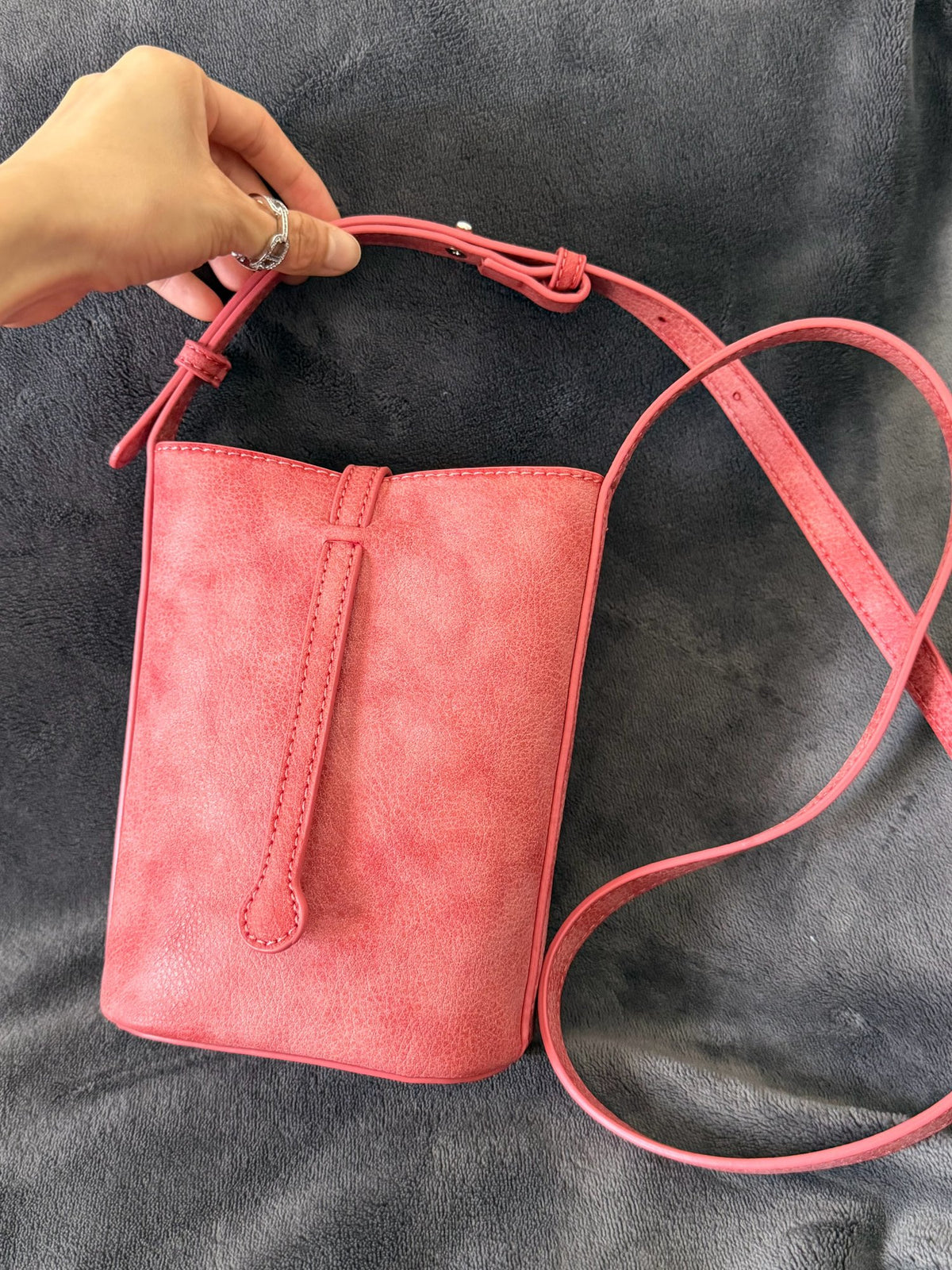 MUGRS Watermelon Red leather phone bag lifted by hand from a grey sofa